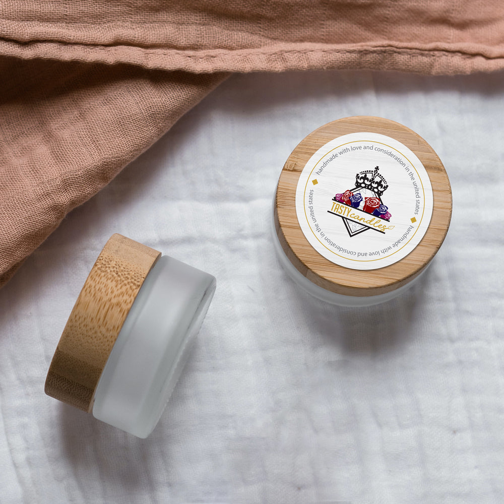 There is a glass candle jar with a custom printed label reading: “Tasty Candles”. The label is white and affixed to a metal jar lid.